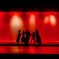 A circle of girls dance in silhouettes against a bright red backdrop.